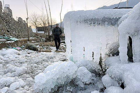 A man walks past icicles hanging from a structure amid heavy frost and snow cover during a cold wave in the valley, in Anantnag district, Jammu and Kashmir.