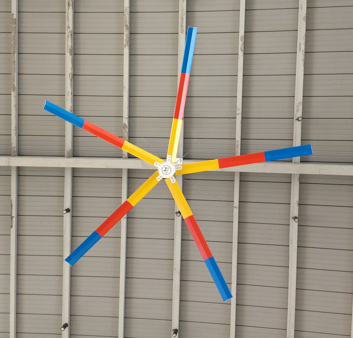 Colorful six-blade industrial ceiling fan mounted in a warehouse roof