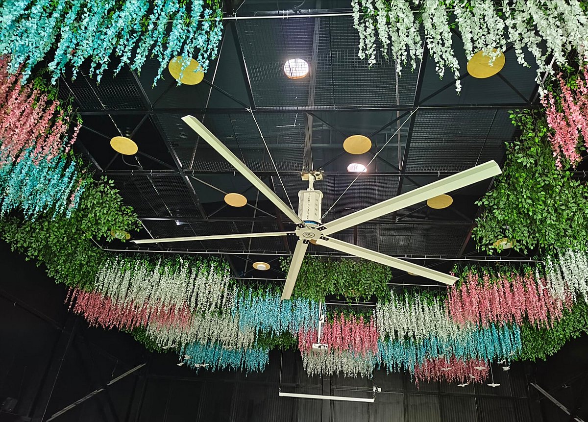 Large white ceiling fan amid hanging greenery and decorative lights indoors