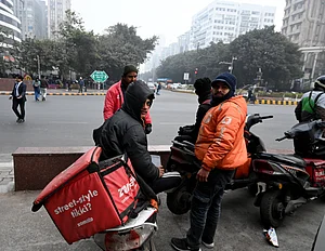 Source: IMAGO / Hindustan Times : Gig workers rest during a nationwide strike at Connaught Place on December 31, 2025 in New Delhi, India. Gig workers are striking on New Year's Eve, demanding better pay, social security, and an end to 10-minute delivery mandates due to safety concerns and stress. While the strike aimed to disrupt high-demand New Year's Eve services, the overall impact was mitigated by aggressive counter-measures from delivery platforms.