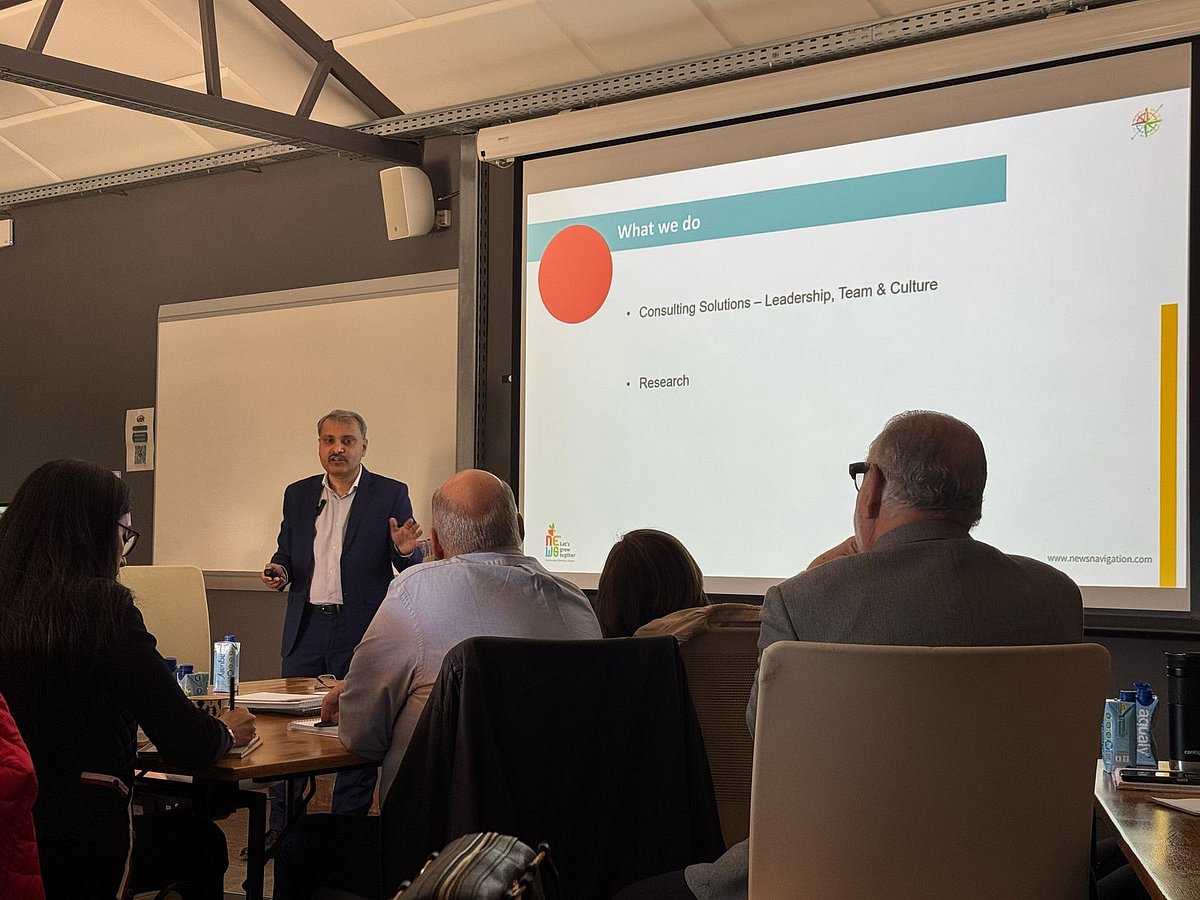 Business professional presenting a slide to a small seated audience in a meeting room