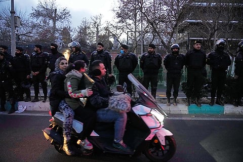 Policemen protect the British Embassy during a protest by hardline supporters of the Iranian government, as people ride on their motorbike in Tehran, Iran.