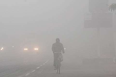 A person cycles through dense fog on a winter morning, in Lucknow.