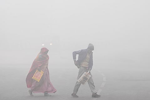 People cross a road amid dense fog during a cold winter morning, in New Delhi. Dense fog shrouded the national capital on Saturday morning, drastically reducing visibility, while the minimum temperature was recorded at 4.4 degrees Celsius, 3.2 notches below the season's average.