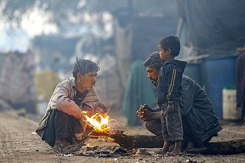 People warm themselves near a bonfire on a cold and foggy morning, in Rajkot.