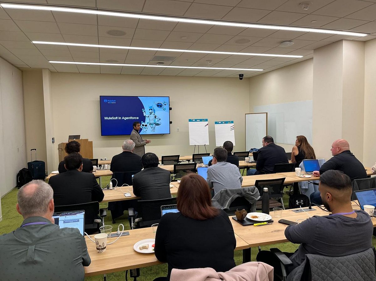 A man in a suit presenting to a group seated around a conference table during a meeting.