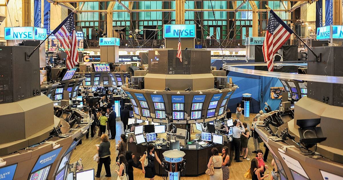 Busy trading floor of the New York Stock Exchange with monitors and American flags.