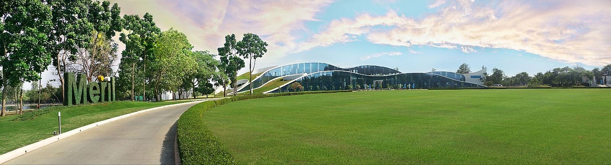 A winding road leads toward a large, modern building with a curved roof nestled in a grassy field.