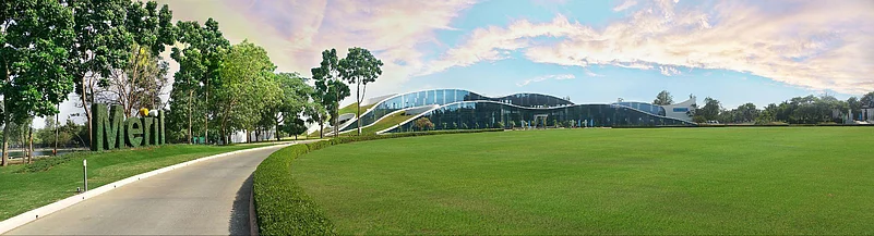 A winding road leads toward a large, modern building with a curved roof nestled in a grassy field.