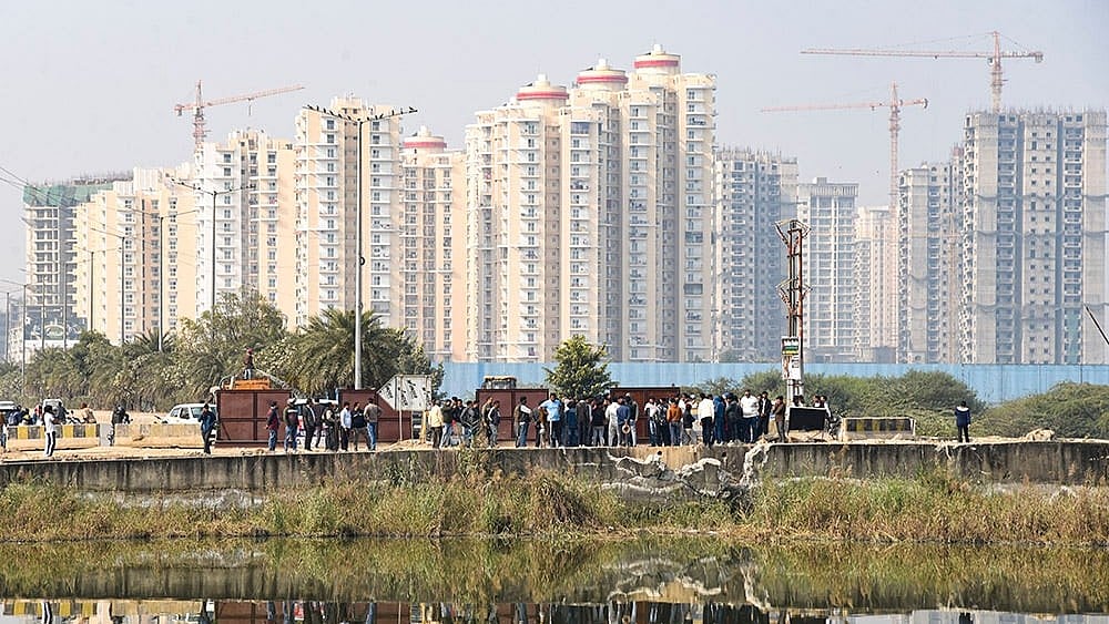 People gather near a water-filled pit at a construction site following the death of a 27-year-old engineer who drowned, in Noida. - | Photo: PTI