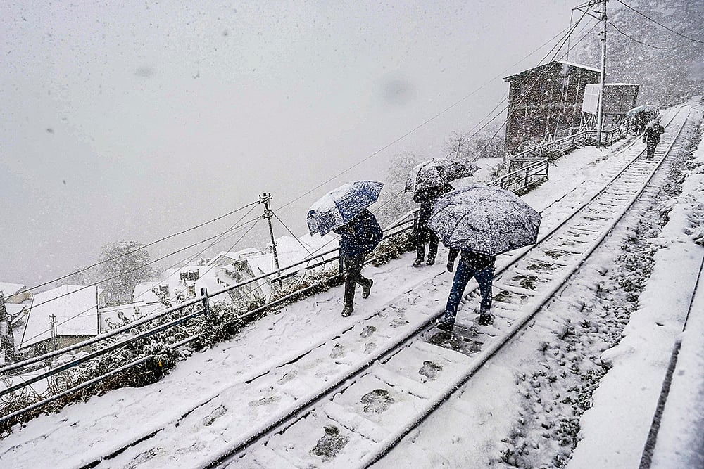 People traverse a snow-covered rail track amid ongoing snowfall, in Shimla. The precipitation aligns with forecasts predicting up to 28 cm of snow on January 23, ending the region's dry spell under active western disturbances. - | Photo: PTI