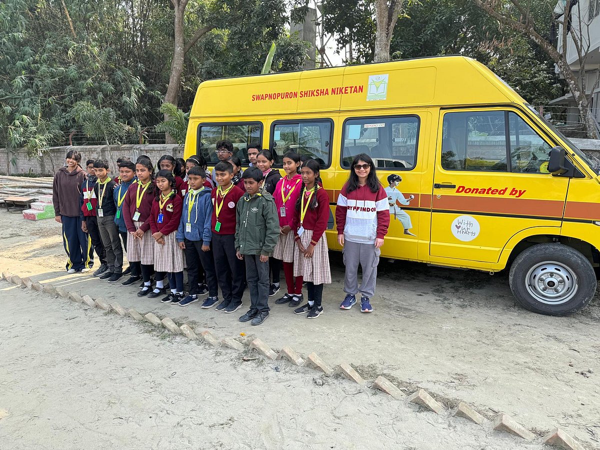 Students and a woman pose by a yellow Swapnopuron Shiksha Niketan school bus