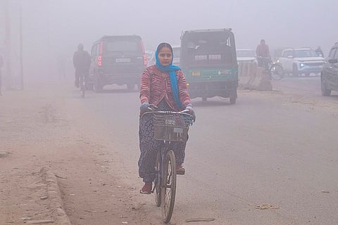 A woman cycles as vehicles pass by amid fog on a winter morning, in Gurugram.