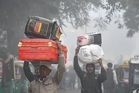 People carry luggage over their heads on a cold and foggy morning, in Prayagraj.