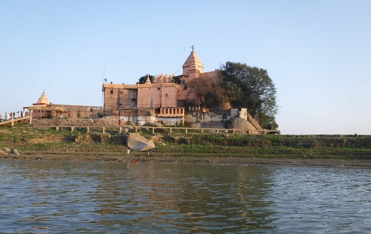An ancient stone temple complex situated on a riverbank under a clear blue sky.