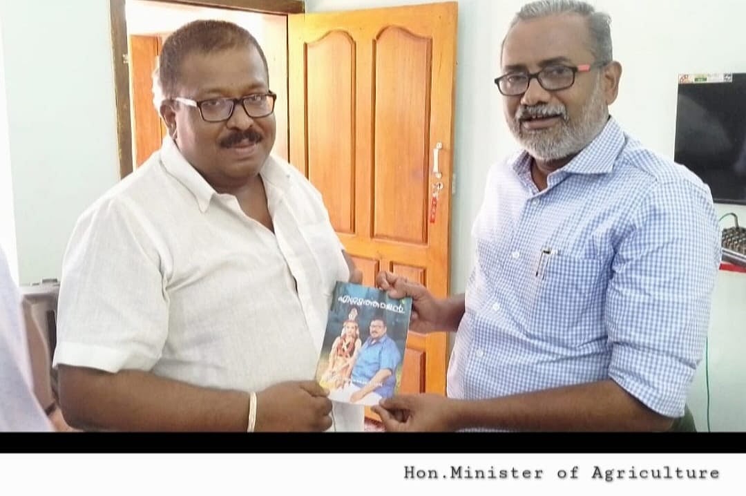 Two men exchanging a book indoors, standing near a wooden door.