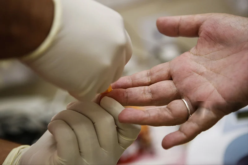 Close-up of a gloved hand performing a finger-prick blood test on a persons finger