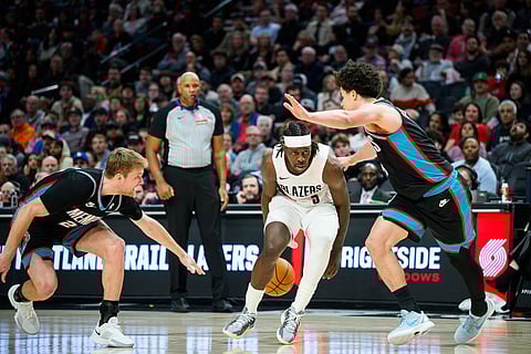Portland Trail Blazers forward Jerami Grant, center, dribbles behind his back as he drives between Memphis Grizzlies guards Cam Spencer, left, and Walter Clayton Jr., right, in the second half of an NBA basketball game in Portland, Oreon.