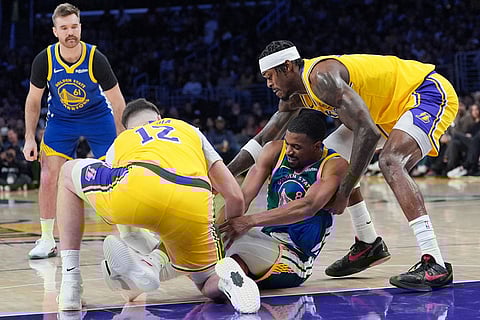 Golden State Warriors guard De'anthony Melton, center, fights for the ball with Los Angeles Lakers forward Jake LaRavia, left, and forward Jarred Vanderbilt during the first half of an NBA basketball game in Los Angeles.
