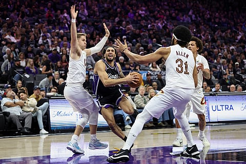 Sacramento Kings guard Devin Carter, center, draws a foul on Cleveland Cavaliers guard Sam Merrill, left, as he goes up for a layup during the first half of an NBA basketball game  in Sacramento, Calif.