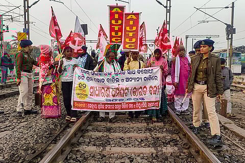 Police personnel stand guard as members of a joint forum of central trade unions shout slogans on a railway track during a nationwide strike called to protest government policies, in Balasore, Odisha.