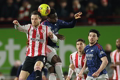 Brentford's Ethan Pinnock, left, and Arsenal's Bukayo Saka jump for the ball during the English Premier League soccer match between Brentford and Arsenal in London.