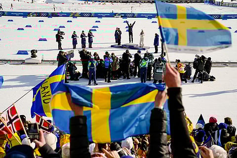 Sweden fans wave flags as Frida Karlsson, of Sweden, jumps on the podium celebrating after winning the gold medal in the cross country skiing women's 10km interval start free at the 2026 Winter Olympics, in Tesero, Italy.