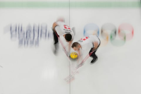 Switzerland's Pablo Lachat-Couchepin and Sven Michel sweep ahead of the stone during a men's curling round robin match against the United States at the 2026 Winter Olympics, in Cortina d'Ampezzo, Italy.