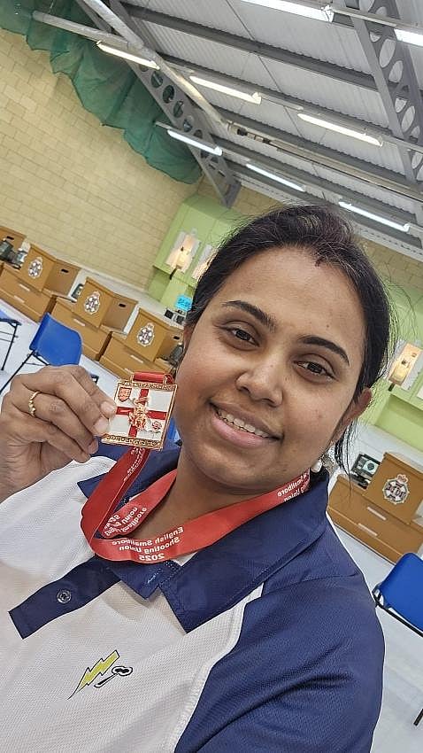 Satabdi Dash holding up a gold medal while smiling in an indoor training facili