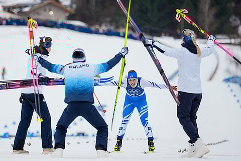 Jasmi Joensuu, of Finland, approaches the finish line and celebrating teammates to win the bronze medal in the cross country skiing women's 4 x 7.5km relay at the 2026 Winter Olympics, in Tesero, Italy.