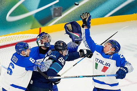Italy's goalkeeper Damian Clara, center, and Italy's Diego Kostner, right, reach for the puck during a preliminary round match of men's ice hockey between Finland and Italy at the 2026 Winter Olympics, in Milan, Italy.