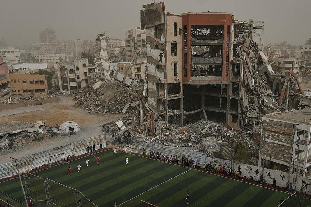 Palestinian players of Gaza Sports Club and Al-Ahly Club take part in a soccer match at a newly constructed field surrounded by buildings destroyed in Israeli ground and air operations, in Gaza City. - | Photo: AP/Jehad Alshrafi