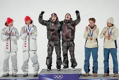 Gold medalists Stephan Embacher and Jan Hoerl, of Austria, celebrate on the podium, with silver medalists Pawel Wasek and Kacper Tomasiak, of Poland, and bronze medalists Kristoffer Eriksen Sundal and Johann Andre Forfang, of Norway, after the ski jumping men's super team competition at the 2026 Winter Olympics, in Predazzo, Italy.