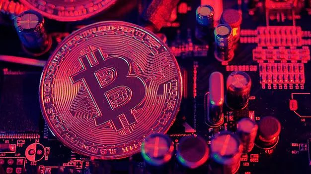 A silver Bitcoin coin resting on an electronic circuit board, illuminated by dramatic red lighting