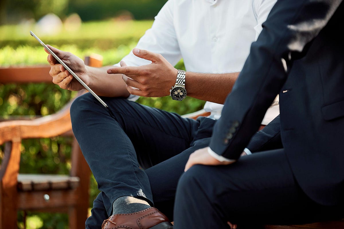Two business professionals sitting on a park bench discussing information on a digital tablet.