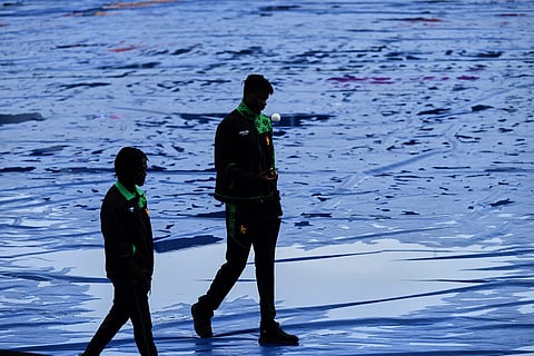 Zimbabwe's Tashinga Musekiwa, right, and Tadiwanashe Marumani walk on the covered ground as rain delayed the start of play during the T20 World Cup cricket match between Ireland and Zimbabwe in Pallekele, Sri Lanka.