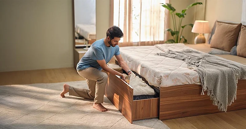 Man pulling out storage drawer under wooden bed in bright bedroom