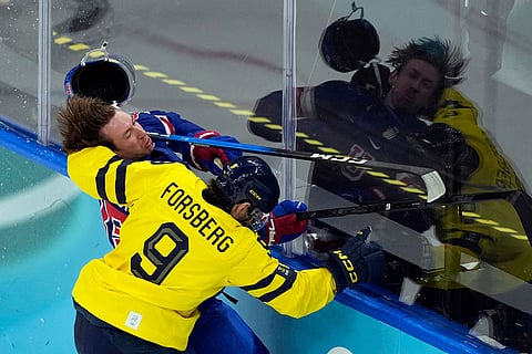 United States' Jake Sanderson (85) loses his helmet as he battles with Sweden's Filip Forsberg (9) during the first period of a men's ice hockey quarterfinal game at the 2026 Winter Olympics, in Milan, Italy.