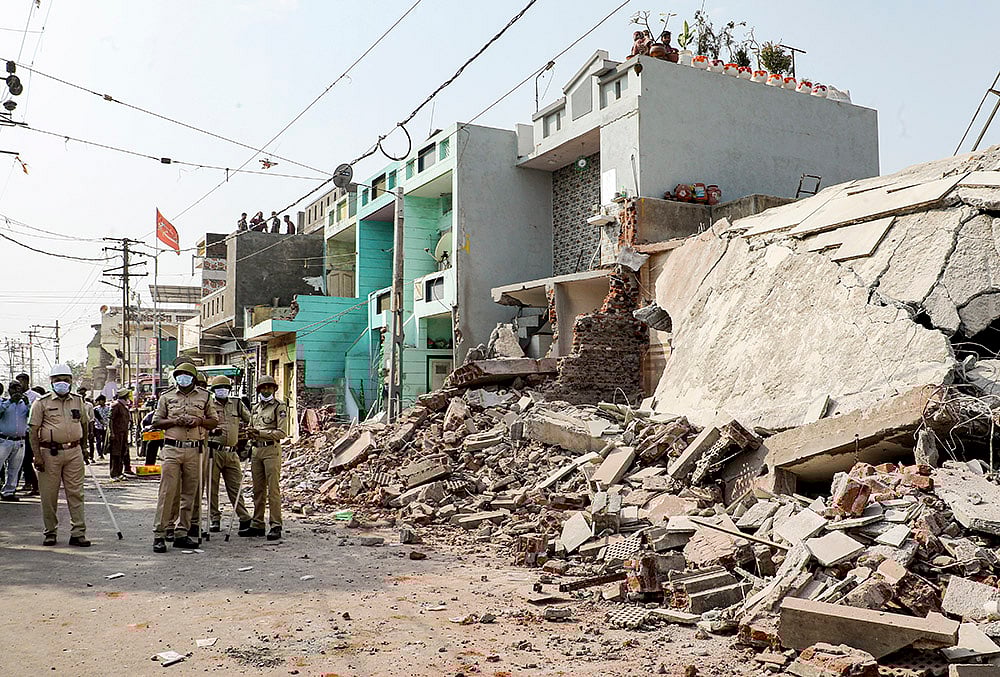Police personnel stands guard as a demolition drive is underway to clear illegal houses along the Aji river banks and TP Road in the Jangleshwar area, in Rajkot, Gujarat. - | Photo: PTI