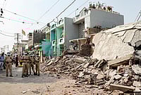 | Photo: PTI : Police personnel stands guard as a demolition drive is underway to clear illegal houses along the Aji river banks and TP Road in the Jangleshwar area, in Rajkot, Gujarat.