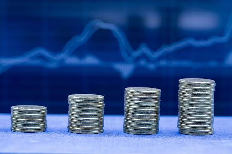 Stacked coins in front of a blue stock graph