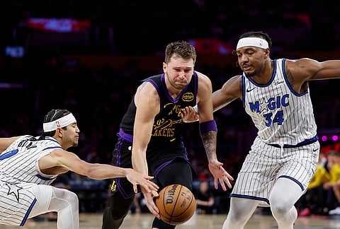 Los Angeles Lakers guard Luka Doncic (77) runs with the ball while being guarded by Orlando Magic guard Anthony Black (0) and Orlando Magic center Wendell Carter Jr. (34) during the second half of an NBA basketball game in Los Angeles.