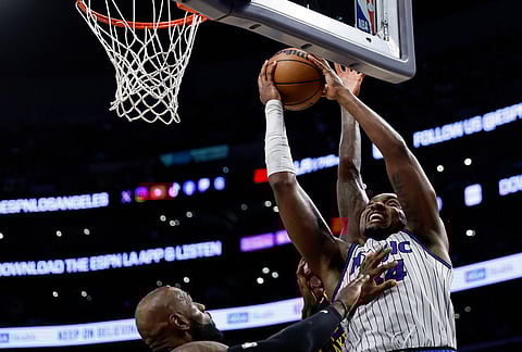 Orlando Magic center Colin Castleton (14) drives to the basket with the ball while being guarded by Los Angeles Lakers forward LeBron James (23) during the first half of an NBA basketball game in Los Angeles. 