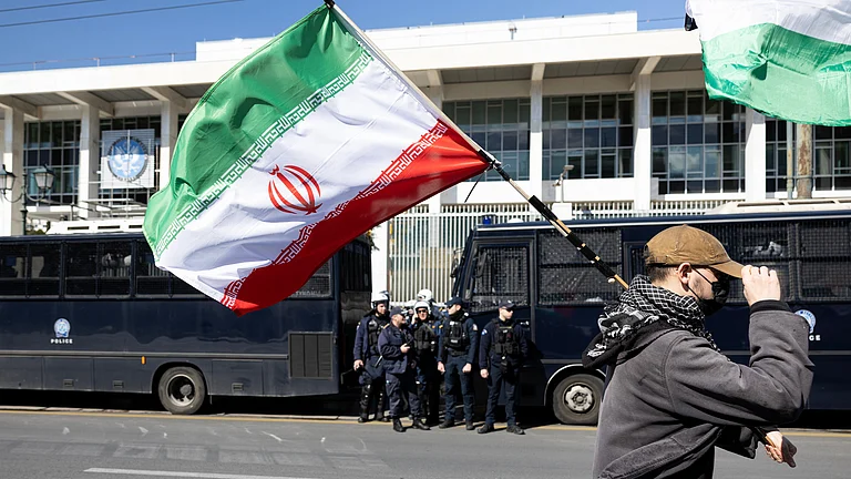 A protester waves an Iranian flag during a rally against U.S. and Israeli strikes on Iran, outside the U.S. embassy in Athens, Greece, Sunday, Mar. 1, 2026. - | Photo: AP/Yorgos Karahalis