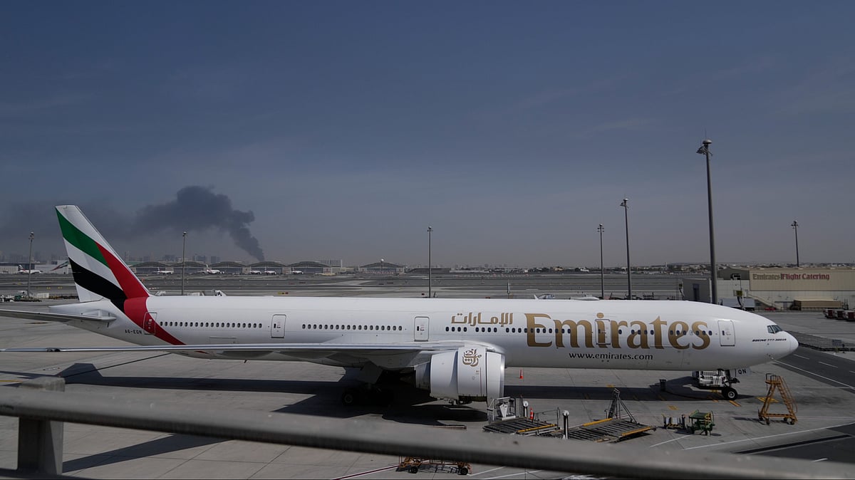 A plume of smoke caused by an Iranian strike is seen in the background an an Emirates plane is parked at the Dubai International Airport after its closure in Dubai, United Arab Emirates, Sunday, March 1, 2026. - Altaf Qadri