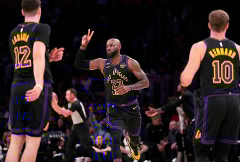 Los Angeles Lakers forward LeBron James, center, gestures after scoring as Los Angeles Lakers forward Jake LaRavia, left, and guard Luke Kennard watch during the first half of an NBA basketball game in Los Angeles.