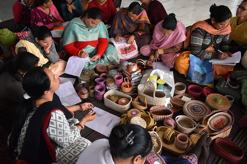 A group of women sitting on the floor weaving baskets and taking notes during a workshop.