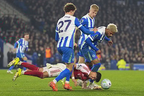 Arsenal's Piero Hincapie falls betweem Brighton's Mats Wieffer, left, and Georginio Rutter during the Premier League soccer match between Brighton and Arsenal in Brighton, England.