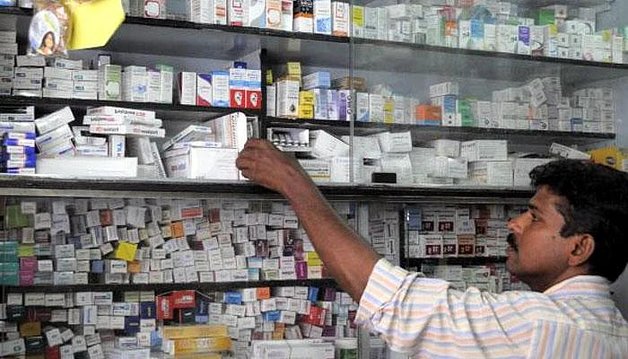 Pharmacist reaching for medicine boxes on shelves inside a crowded pharmacy