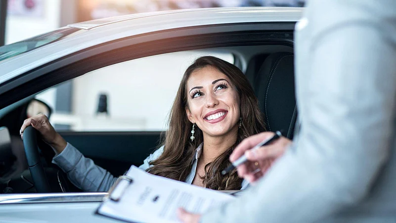Woman in car smiling while receiving documents from a person outside